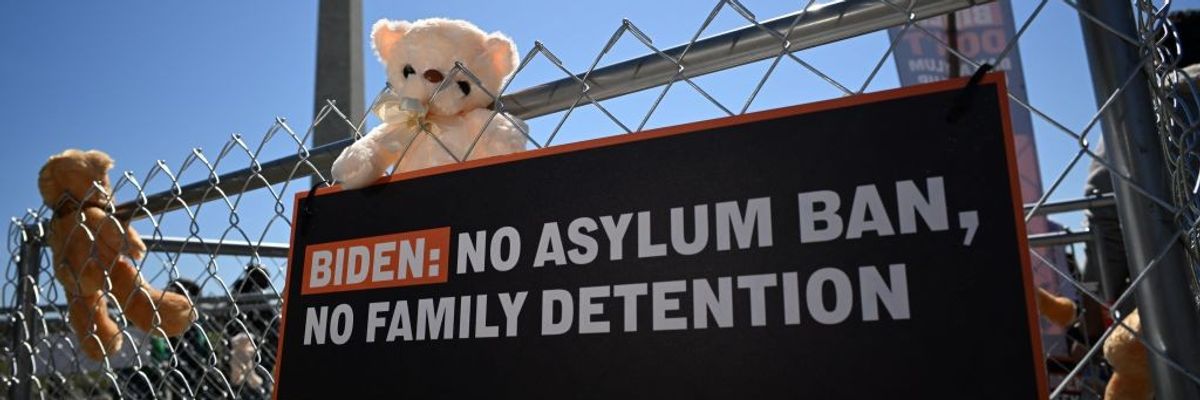 A sign and teddy bears are tied to a fence as immigrant rights organizations rally