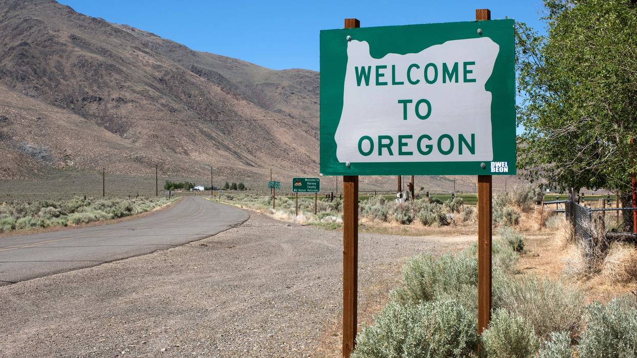 A sign reads "Welcome to Oregon" along a two-land country road with a mountainout backdrop.