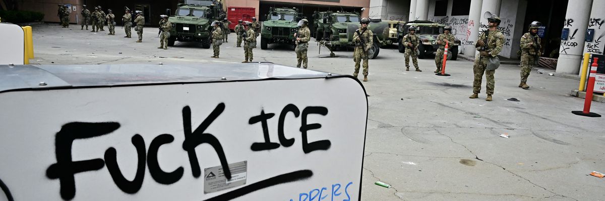 A sign says "Fuck ICE" in front of National Guard members deployed in LA.