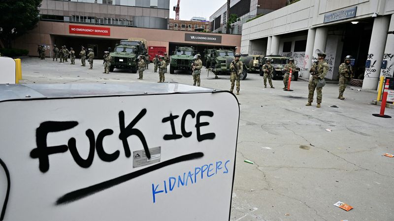 A sign says "Fuck ICE" in front of National Guard members deployed in LA.