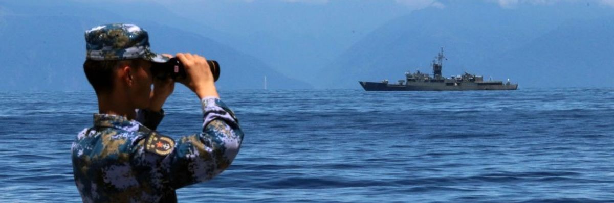 A soldier looks through binoculars at a naval ship on the water.