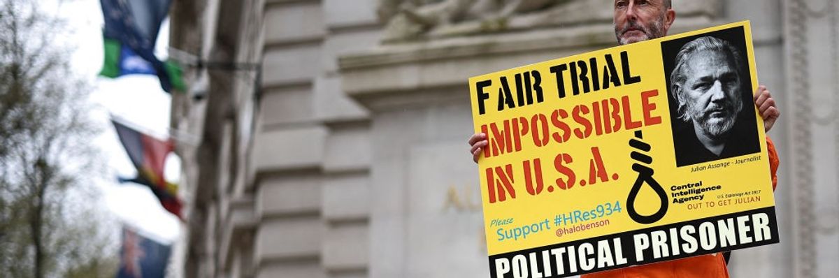 A supporter of Julian Assange carries a yellow sign reading "Fair Trial Imopossible in USA)