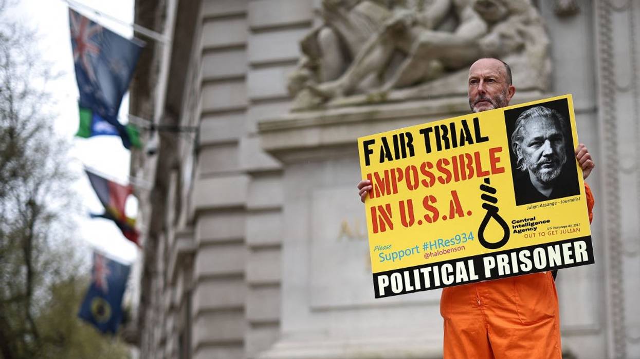 A supporter of Julian Assange carries a yellow sign reading "Fair Trial Imopossible in USA)