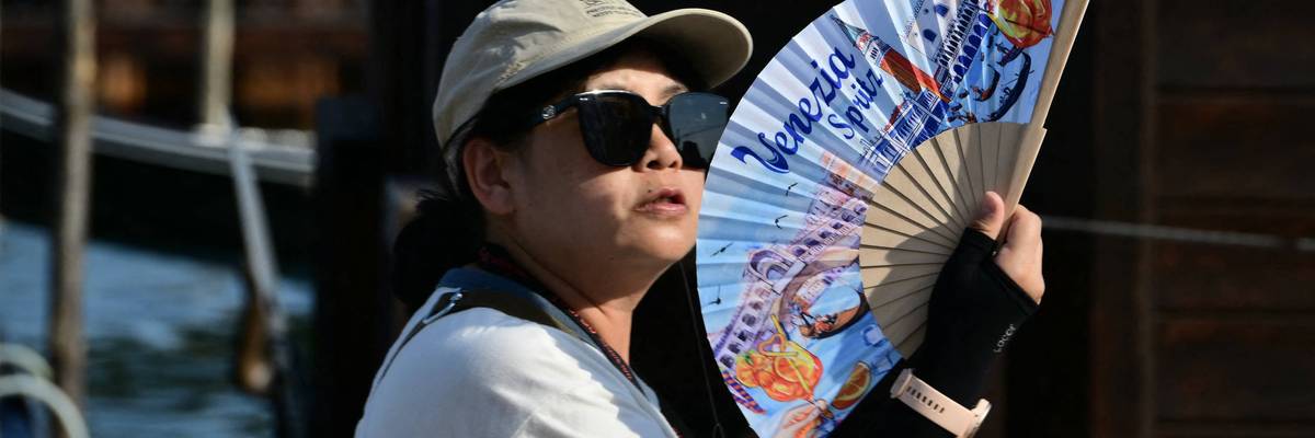 A tourist uses a hand fan to cool herself