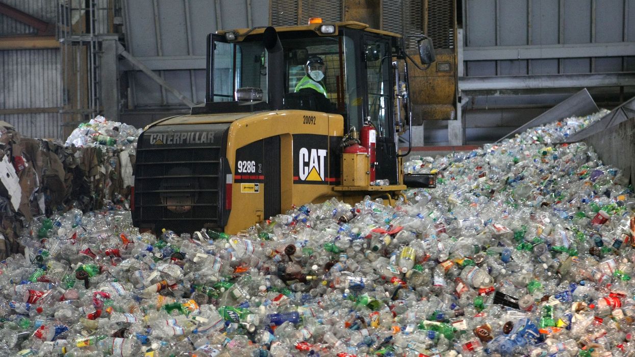 A tractor drives through a giant pile of plastic bottles