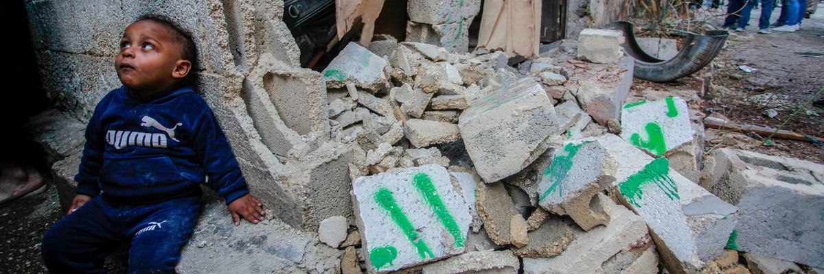 A traumatized Palestinian todder sits on a pile of rubble