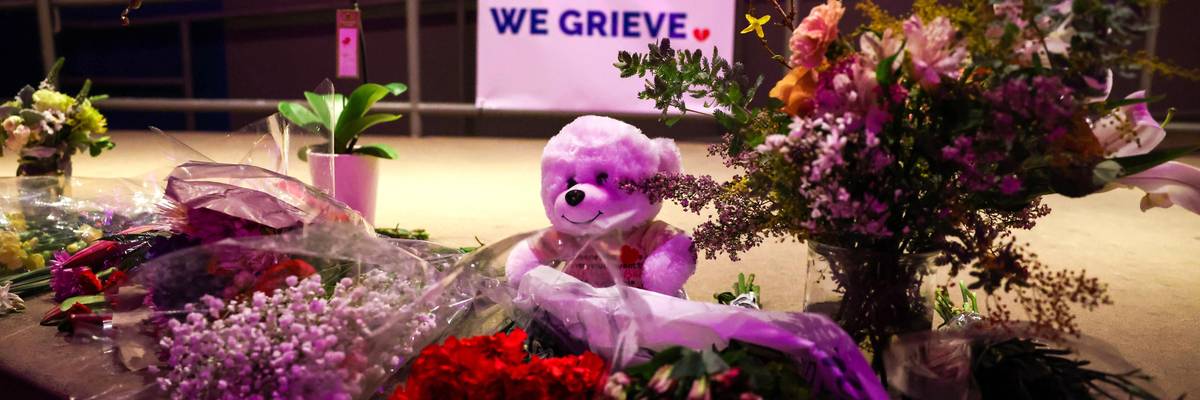 A tribute banner is displayed along with seven candles and flowers in a makeshift memorial