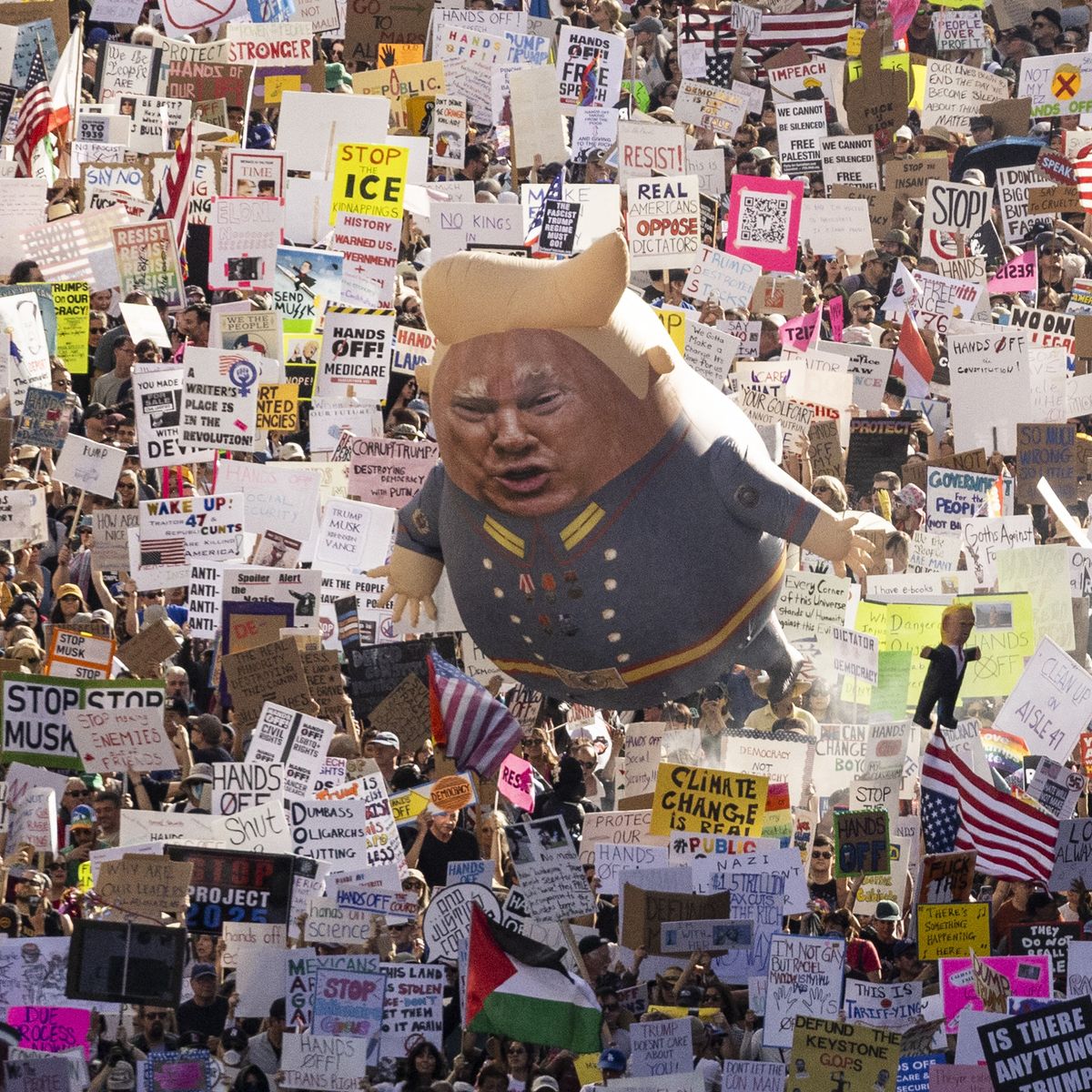 A Trump balloon floats above signs at a protest.