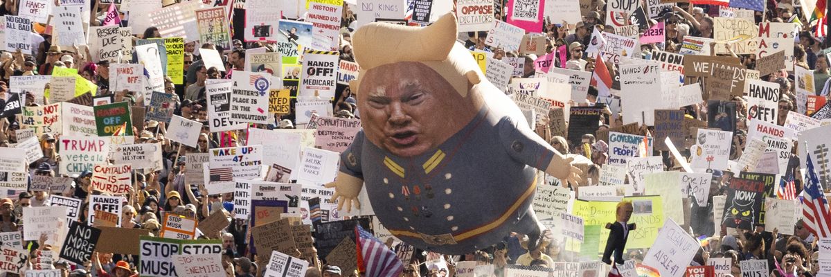 A Trump balloon floats above signs at a protest.