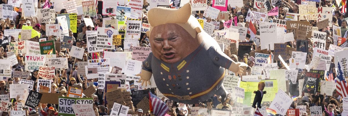 A Trump balloon floats above signs at a protest.