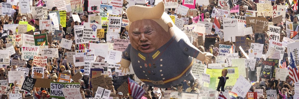 A Trump balloon floats above signs at a protest.
