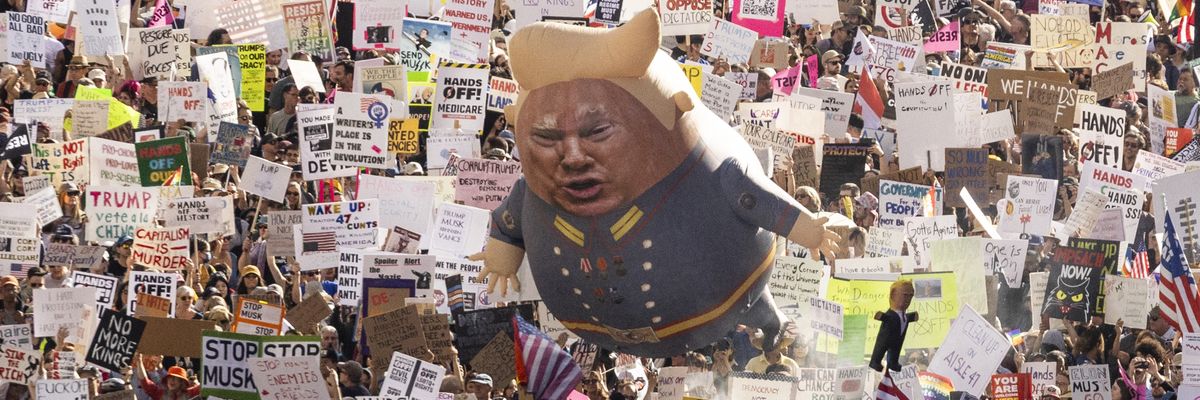 A Trump balloon floats above signs at a protest.