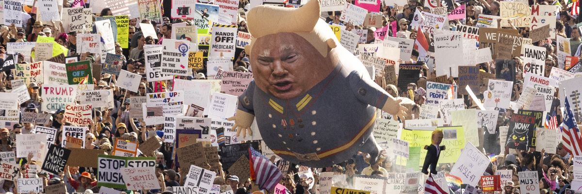 A Trump balloon floats above signs at a protest.