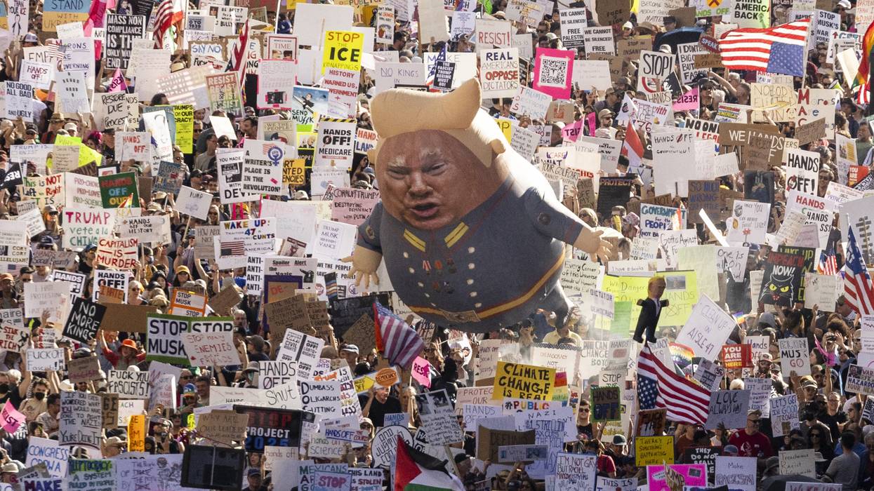A Trump balloon floats above signs at a protest.