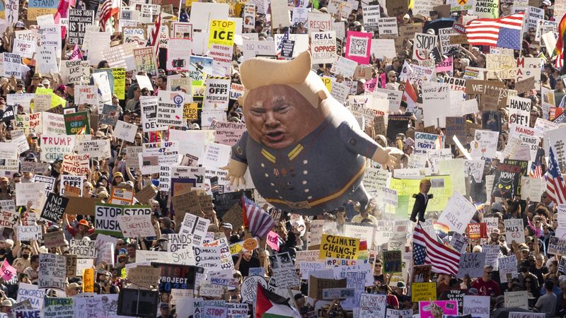 A Trump balloon floats above signs at a protest.