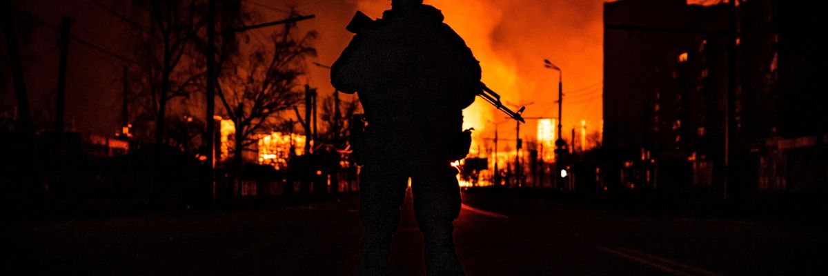 A Ukraine soldier silhouetted agains burning fires following Russian invasion in 2022