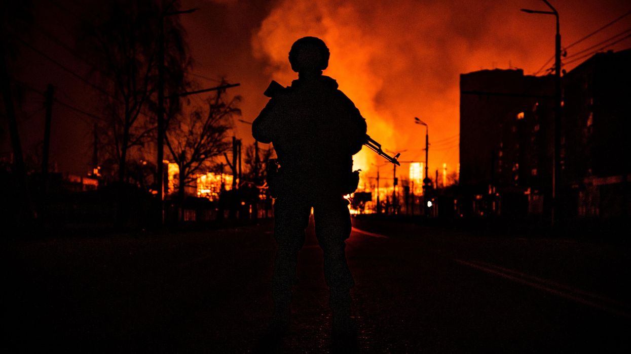 A Ukraine soldier silhouetted agains burning fires following Russian invasion in 2022