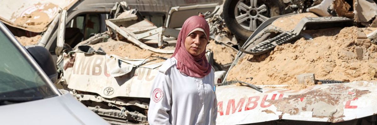 A veiled female Palestinian Red Crescent paramedic walks by a row of bombed ambulances in Gaza