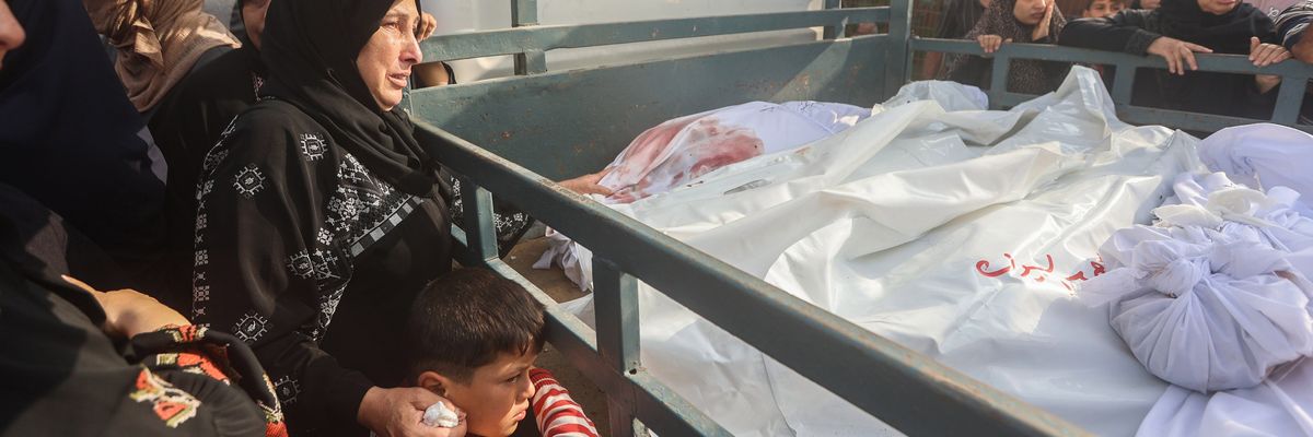 A veiled woman in black and a child sadly view a truckload of Palestinian bodies wrapped in white sheets