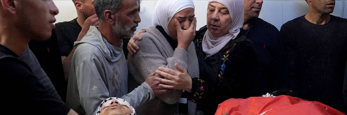 A weeping, grieving Palestinian woman is consoled over the bodies of a man and boy killed by Israeli forces
