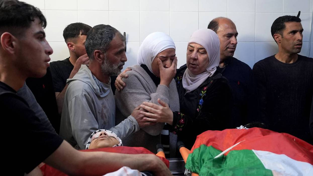 A weeping, grieving Palestinian woman is consoled over the bodies of a man and boy killed by Israeli forces