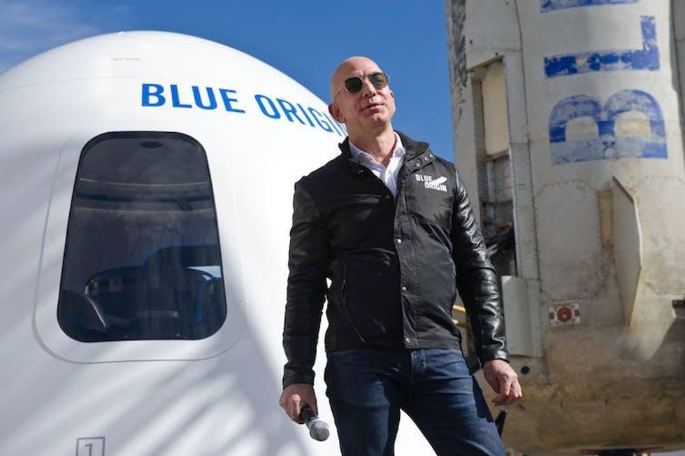 A white man stands in front of a rocket reading 'BLUE ORIGIN'