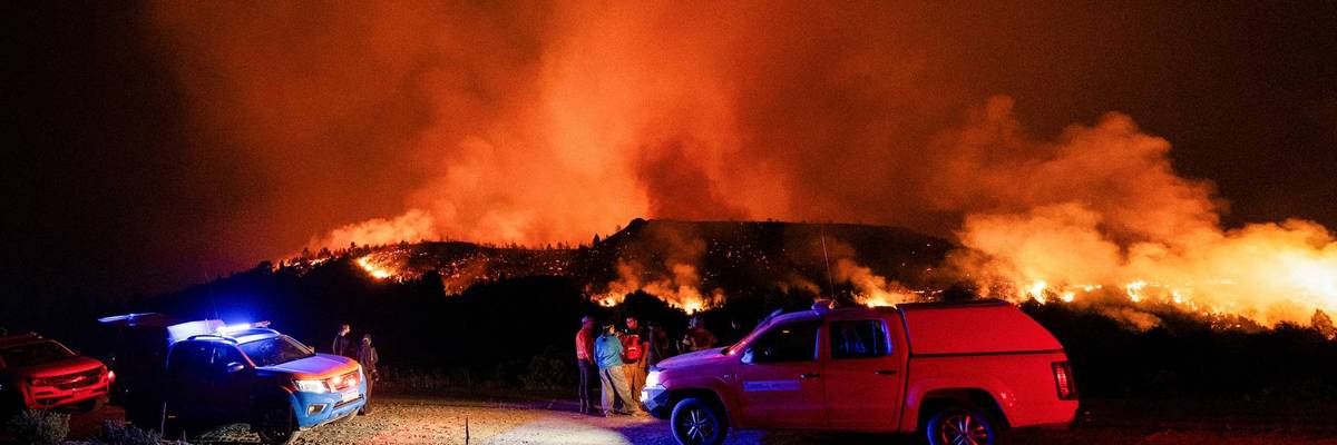 A wildfire burns in hills behind emergency vehicles.