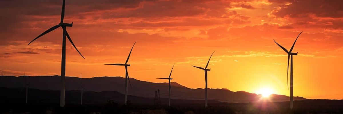 A wind farm is show in front of mountains at sunset.