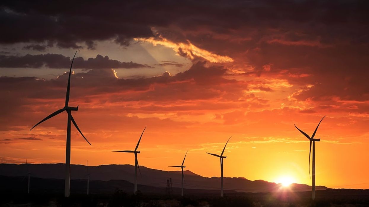 A wind farm is show in front of mountains at sunset.