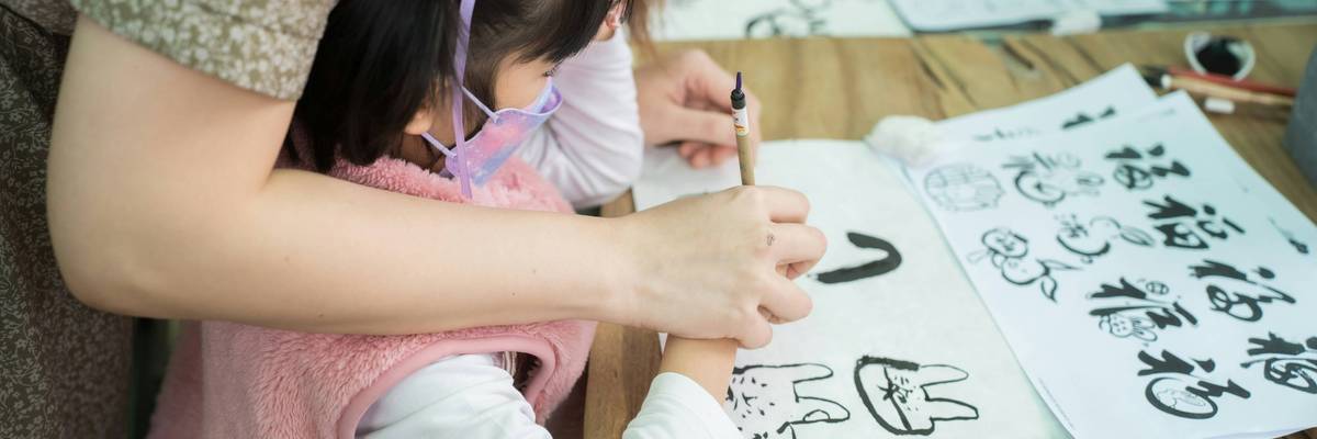 A woman and a little girl write on a piece of paper.