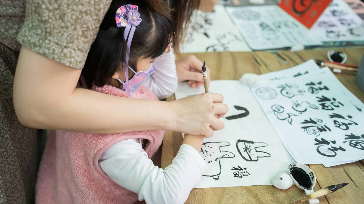 A woman and a little girl write on a piece of paper.
