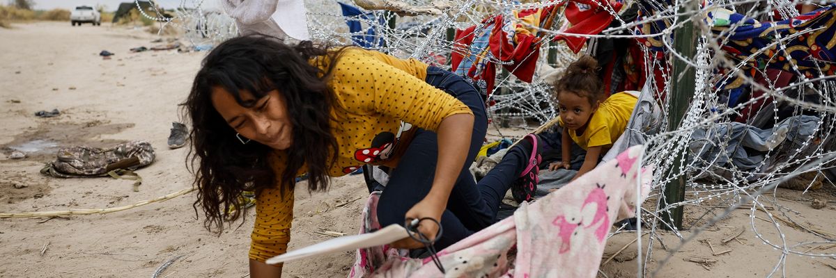 A woman and child crawl through razor wire 