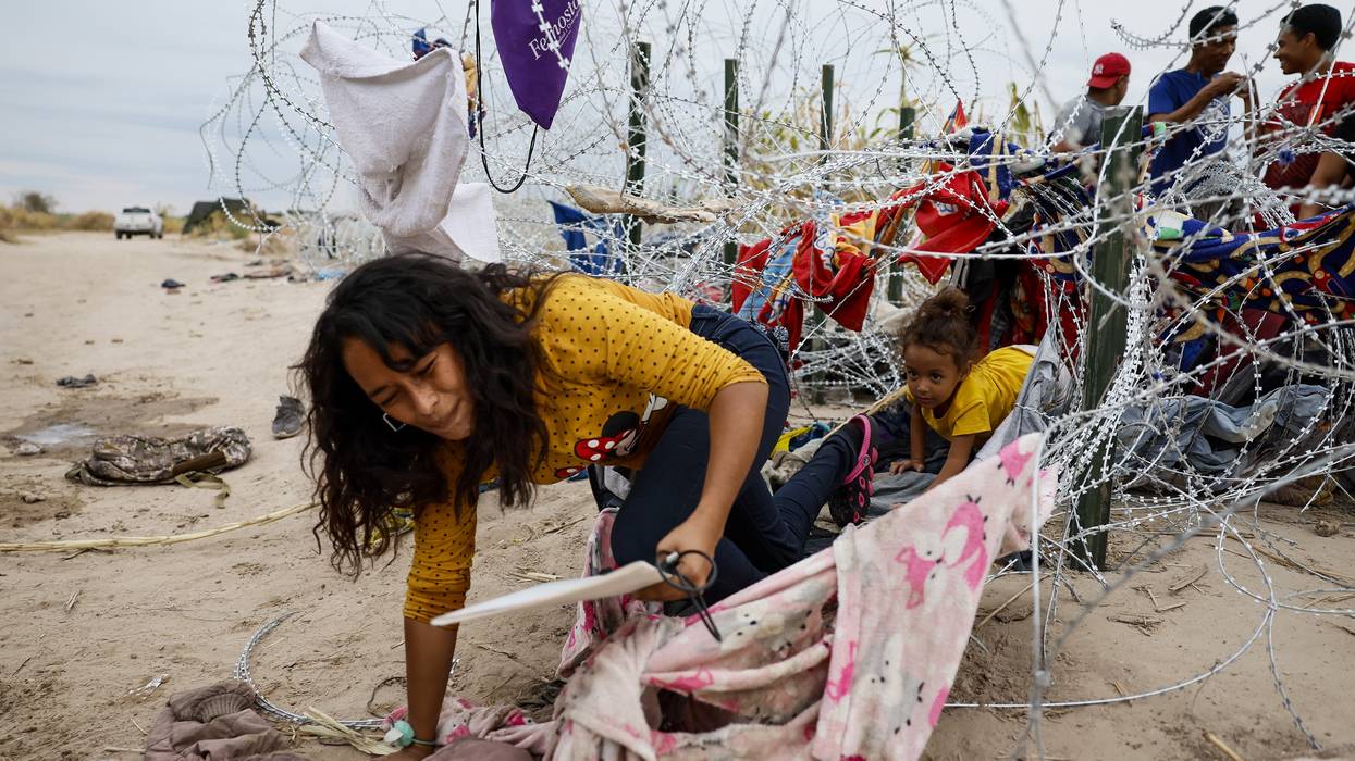A woman and child crawl through razor wire