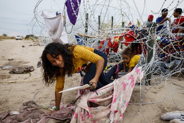 A woman and child crawl through razor wire