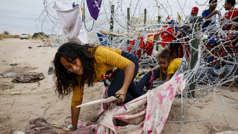 A woman and child crawl through razor wire