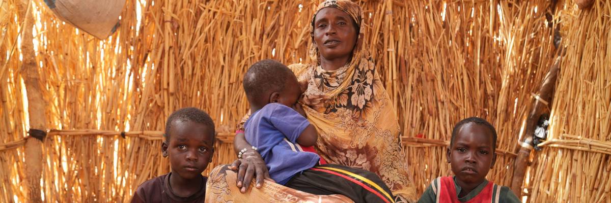 A woman and her children sit in a shack at a displacement camp near the border town Al-Tina in western Sudan