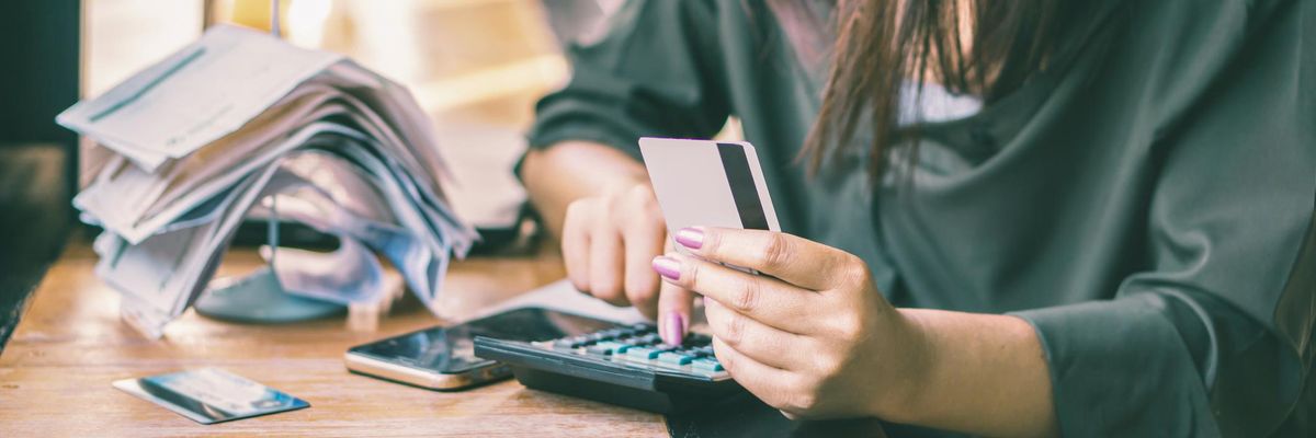 A woman calculates expenses and debt from credit cards with bills in background.