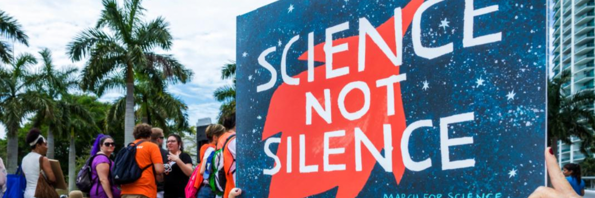 A woman carries a sign reading "Science not Silence"