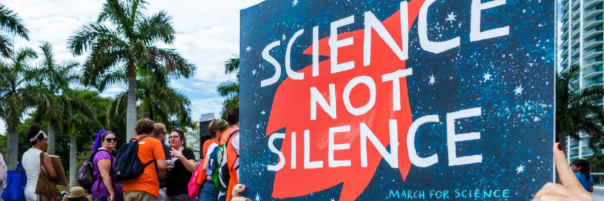 A woman carries a sign reading "Science not Silence"