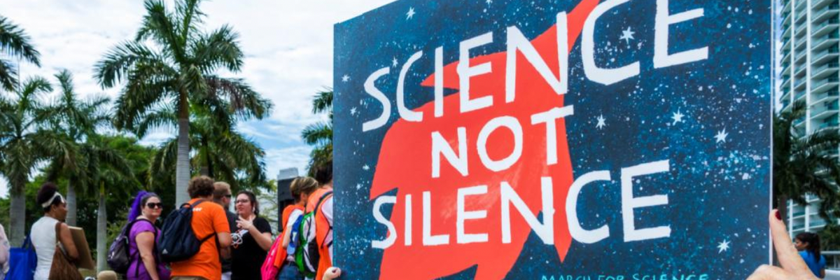 A woman carries a sign reading "Science not Silence" 