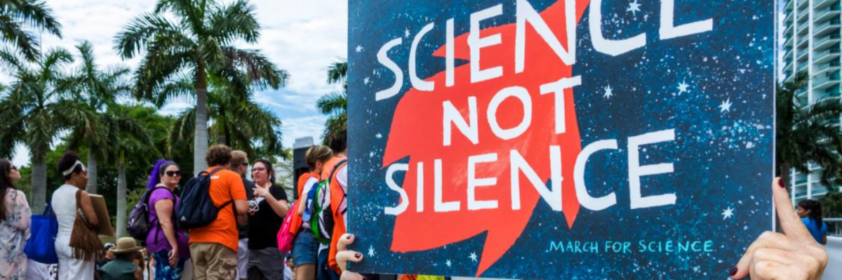 A woman carries a sign reading "Science not Silence" 