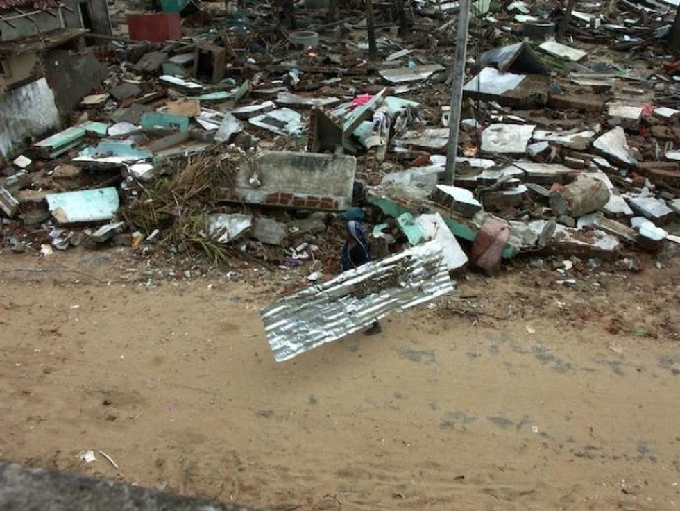 A woman carries a tin sheet in Kalmunai, a city in the Ampara District in Sri Lanka's Eastern Province. Some 3,500 people living in three villagers on the eastern coast lost their lives - comprising a tenth of the national death toll. They were mostly poor fishermen living in humble homes next to the sea. (Photo: Amantha Perera/IPS)