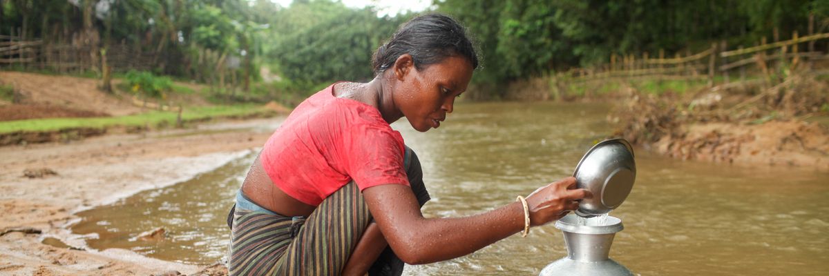 A woman collects clean drinking water by digging a hole at a mountain ridge in Netrokona District, Bangladesh