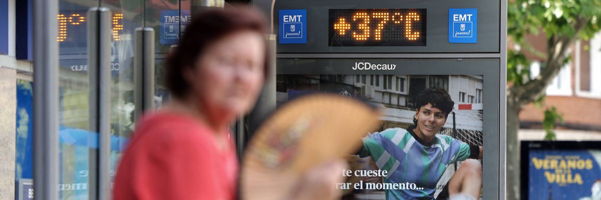 A woman fans herself by a sign reading 37 degrees Celsius, or 99 degrees Fahrenheit