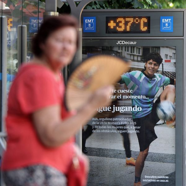 A woman fans herself by a sign reading 37 degrees Celsius, or 99 degrees Fahrenheit