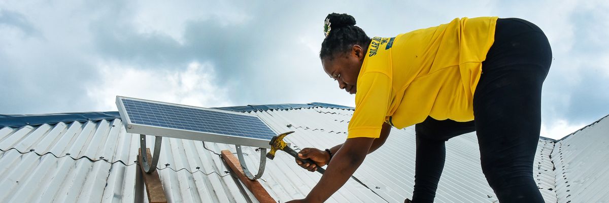 A woman fixes a rooftop solar panel in Cameroon.