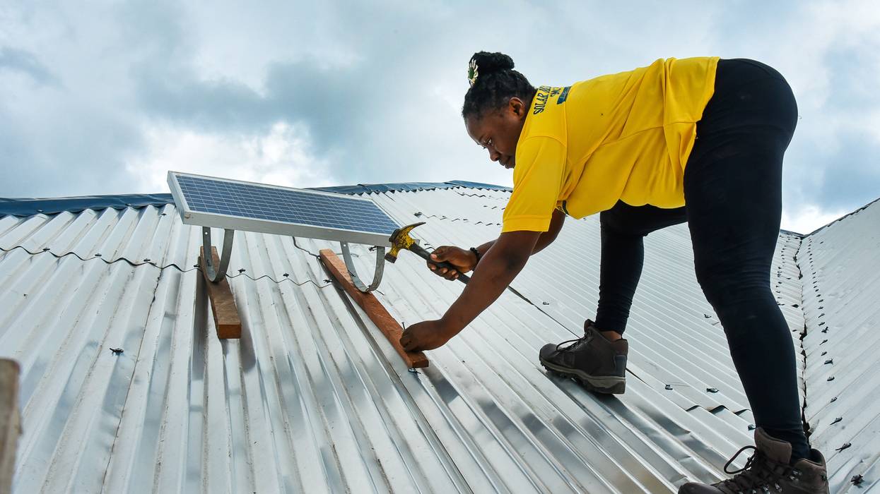 A woman fixes a rooftop solar panel in Cameroon.