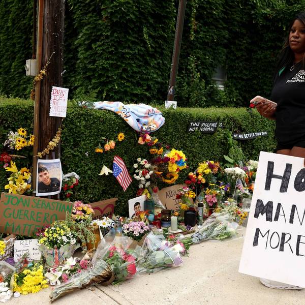 A woman holding a "How Many More?" sign visits a memorial in Maine