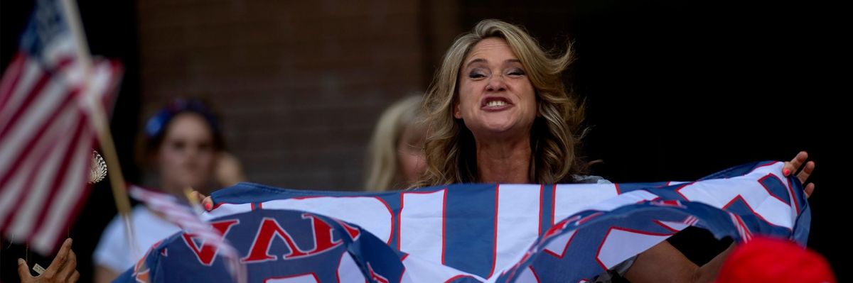 A woman holding a Trump flag reacts to a male driver in a passing car waving a Biden-Harris flag at an America First" rally.