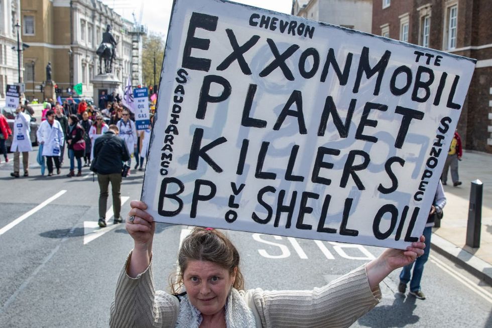 A woman holds a black-and-white sign calling the major fossil fuel companies planet killers.